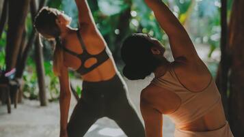 Dos personas practicando yoga en una habitación con vistas a zonas verdes.