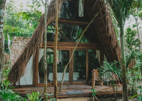 A thatched-roof structure with a stone wall, wooden deck, and glass doors leading to a room.