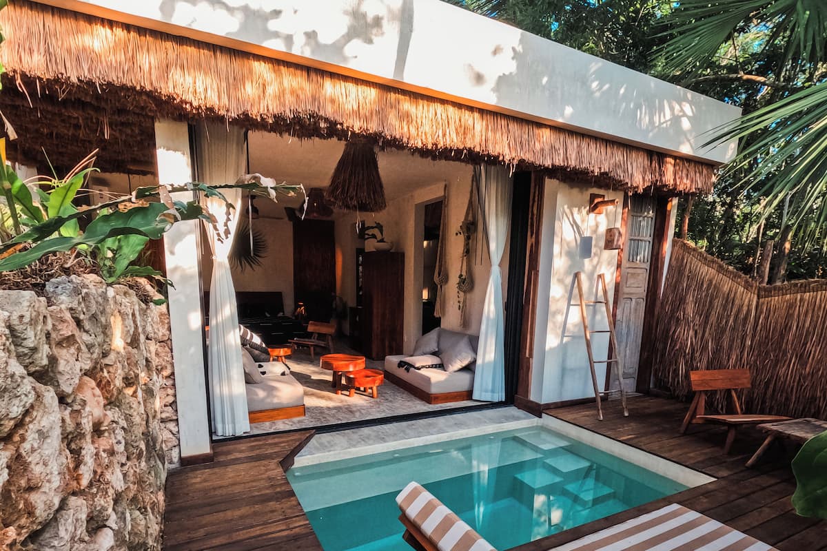 Un espace piscine extérieur moderne, doté d’une terrasse en bois, de chaises longues et d’une structure à toit de chaume.