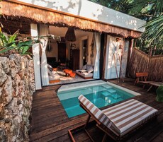 A modern outdoor pool area with wooden decking, lounge chairs, and a thatched-roof structure.