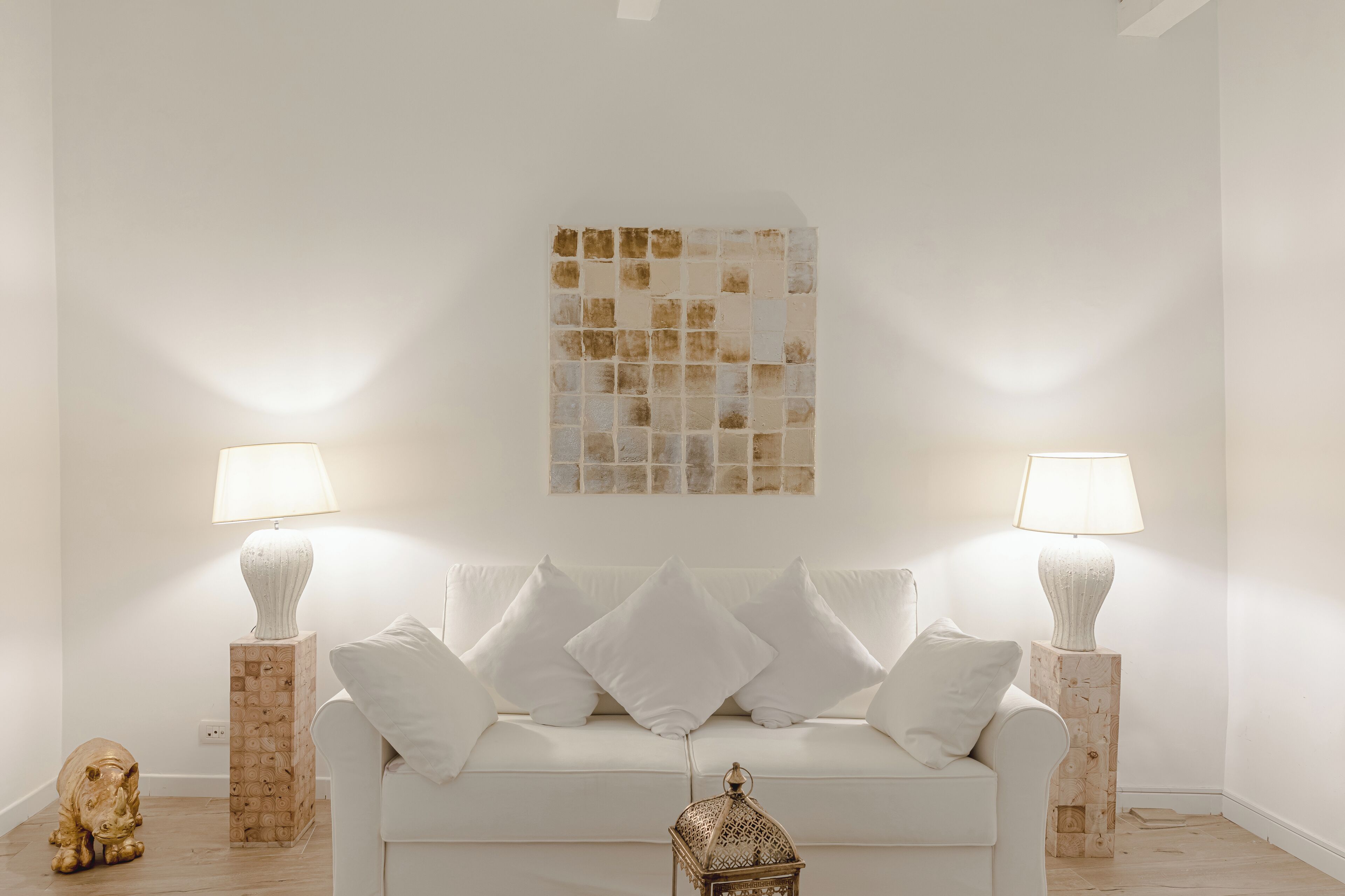 Ein weißes Sofa mit vier Kissen, zwei Beistelltischen mit Lampen, einer dekorativen Tierventil und einem Wandbild.