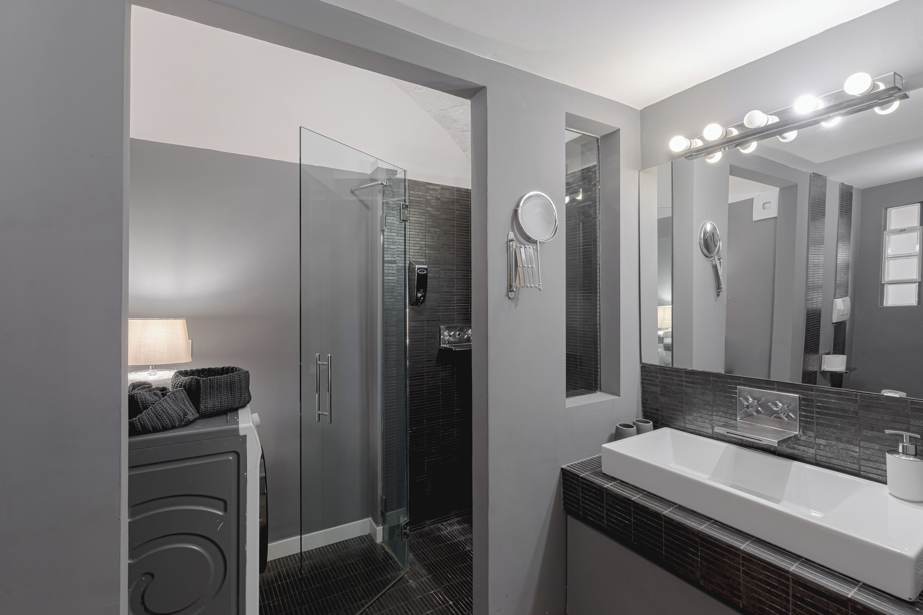 Une salle de bain moderne avec une douche à parois de verre, un grand miroir avec éclairage intégré et un lavabo blanc.