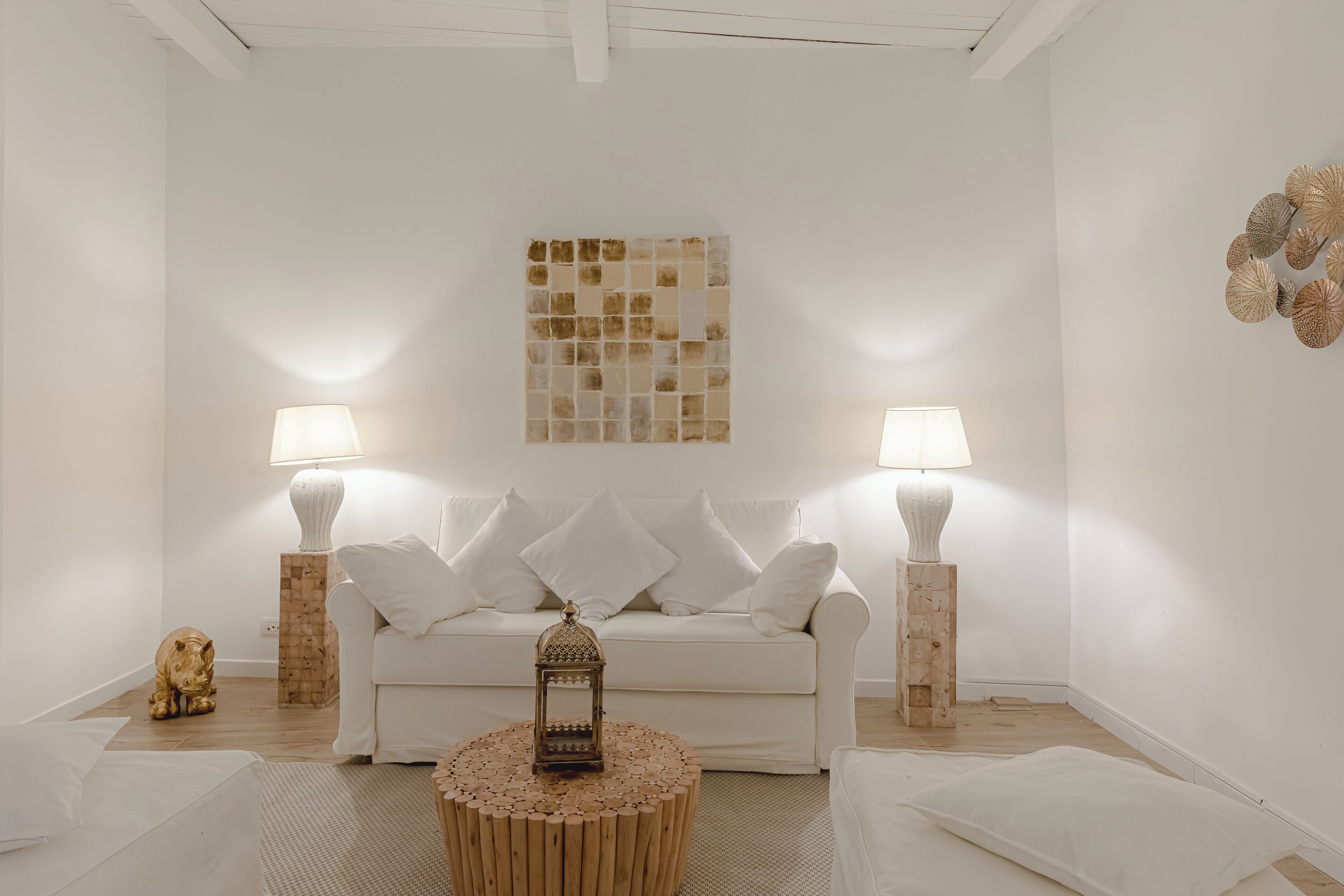 A minimalist living room with a white sofa, two lamps, a decorative wall piece, and a wooden floor.