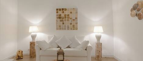 A minimalist living room with a white sofa, two lamps, a decorative wall piece, and a wooden floor.