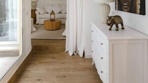 Een kamer met een witte bank, een ronde houten salontafel, een witte dressoir en een groot raam.