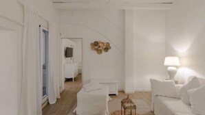 Een witte kamer met een bed, een nachtkastje, een lamp en een decoratie aan de muur.