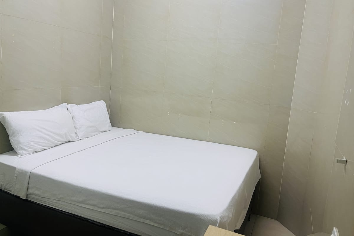 A small, clean room with a single bed, white bedding, and light-colored walls.
