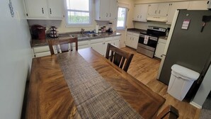 A kitchen with white cabinets, a wooden dining table, and a refrigerator. - Tis’ Time Hideaway. Just a few blocks from beautiful Lake Erie!  (Conneaut)