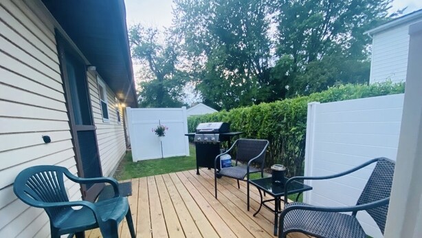 A wooden deck with outdoor furniture, a grill, and a white fence. - Tis’ Time Hideaway. Just a few blocks from beautiful Lake Erie!  (Conneaut)