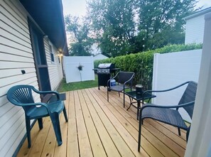 Une terrasse en bois avec des meubles d’extérieur, un barbecue et une clôture blanche.