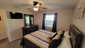 A bedroom with a bed, a ceiling fan, a dresser, a TV, and a window with curtains. - Tis’ Time Hideaway. Just a few blocks from beautiful Lake Erie!  (Conneaut)