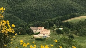 Landskab med huse omgivet af marker og bjerge i baggrunden.