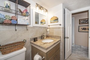 Une salle de bain avec un lavabo blanc, un miroir, un panier et un porte-serviettes.