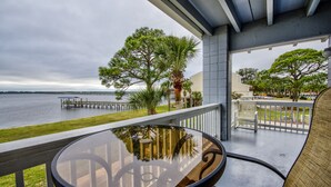 Ein Balkon mit Glastisch und Stühlen, mit Blick auf ein Gewässer und einen entfernten Steg.