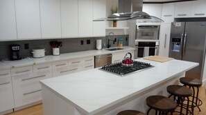 Une cuisine moderne avec des meubles blancs, un îlot central doté de tabourets, une hotte en acier inoxydable, un four et un réfrigérateur.