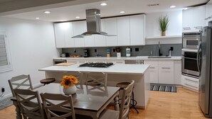 Una cocina moderna con armarios blancos, una isla central, electrodomésticos de acero inoxidable y un comedor con sillas de madera y un jarrón de girasoles.