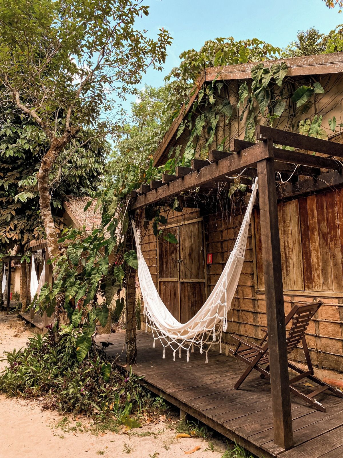 A wooden structure with a hammock, surrounded by greenery and trees.