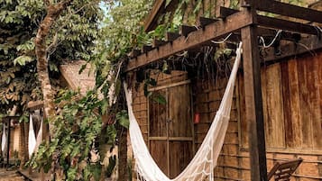 A wooden structure with a hammock, surrounded by greenery and trees.