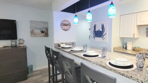 Una cocina moderna con encimera de granito, lámparas colgantes, un reloj y una decoración de cangrejo en la pared.