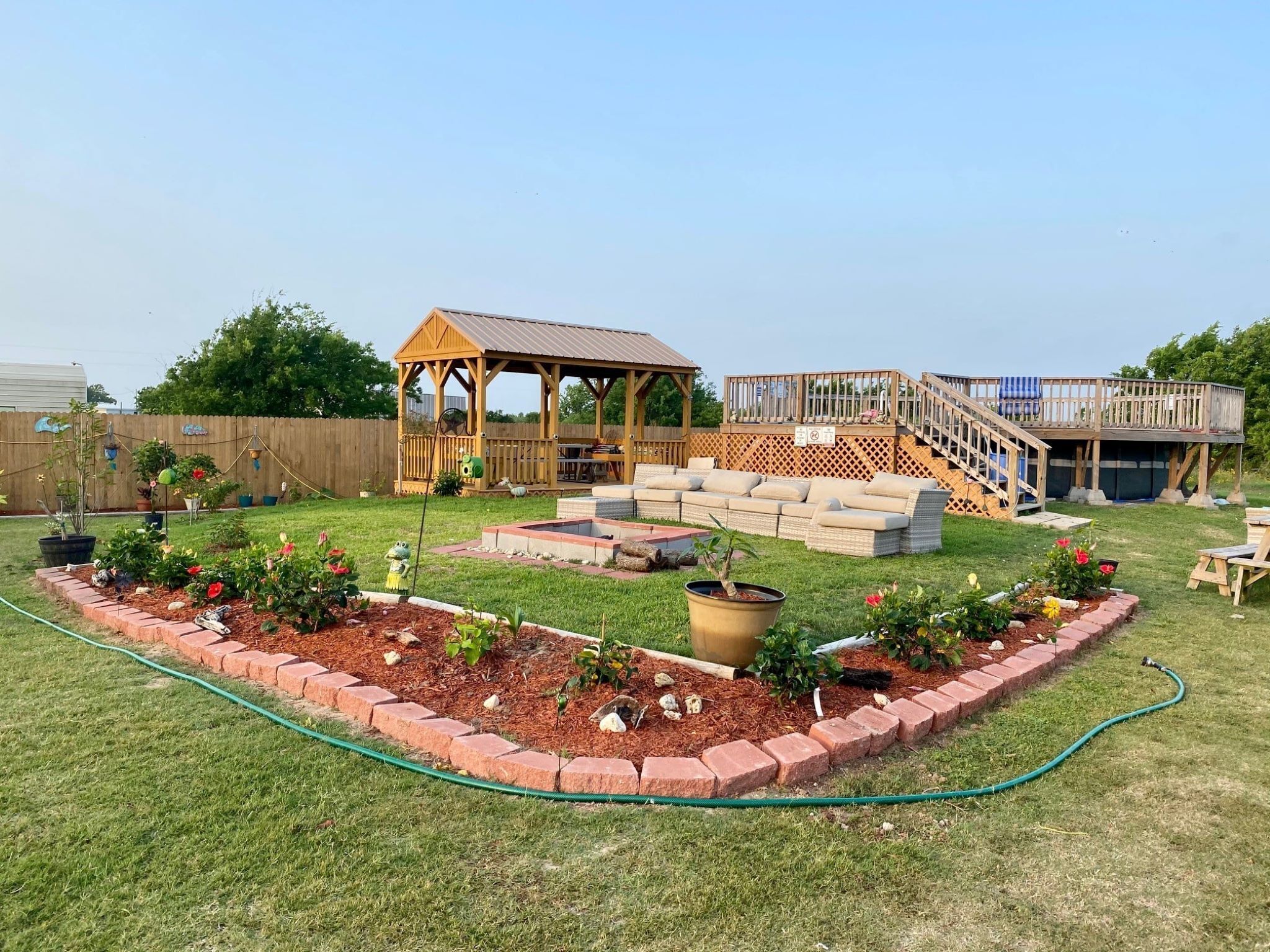 A backyard with a wooden deck, a covered seating area, and a raised platform with a railing.