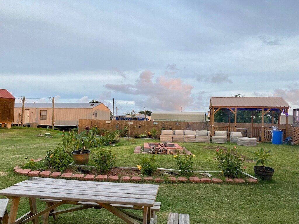 Un jardin avec une table en bois, un foyer et un espace salon abrité.