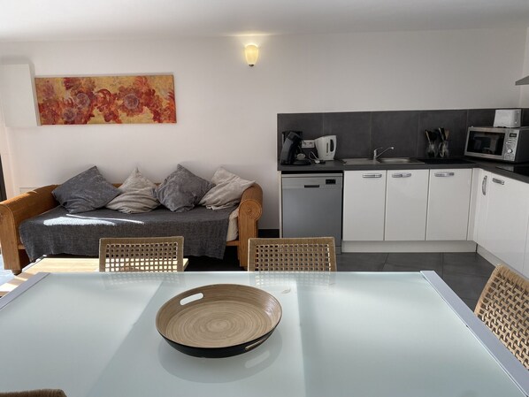 Une cuisine moderne avec des meubles blancs, un four à micro-ondes et une machine à café. On y trouve également un coin repas avec une table en verre et des chaises en osier.