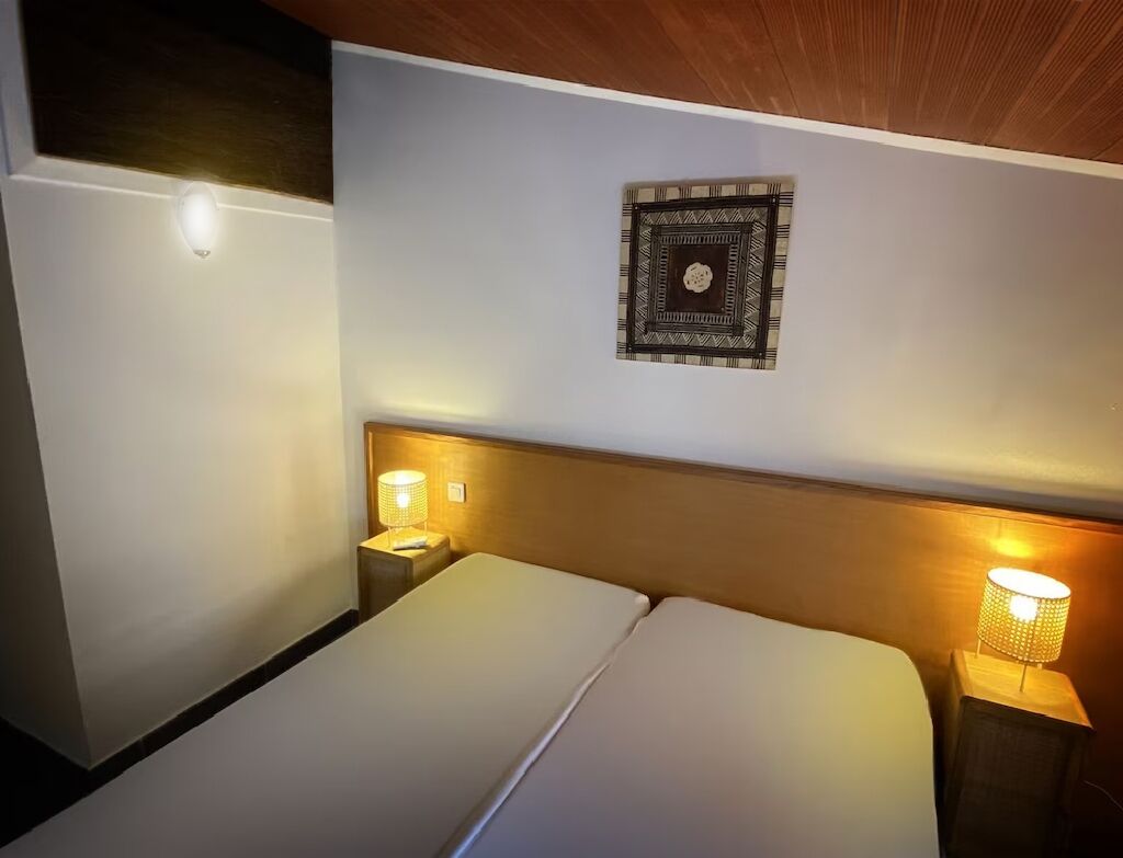 A hotel room with a bed, two bedside tables with lamps, a wall clock, and a wooden ceiling.