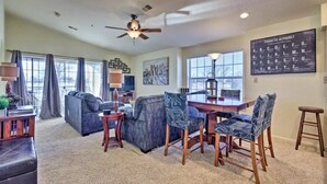 A spacious living room with a ceiling fan, a dining area with a table and chairs, and large windows. - Family-Friendly Branson Condo w/ Outdoor Pool! (Branson)