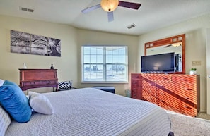 Un dormitorio con cama, cómoda, televisor y ventana con persianas.