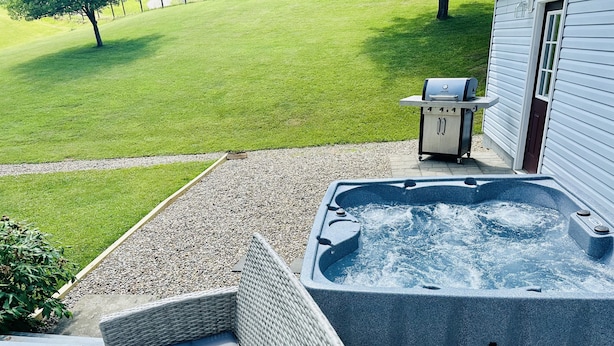 Un bain à remous situé à côté d’une maison, avec une cour gazonnée et un espace patio.