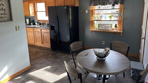 Une cuisine avec des meubles de rangement en bois, un réfrigérateur noir et un coin repas comprenant une table ronde et des chaises.