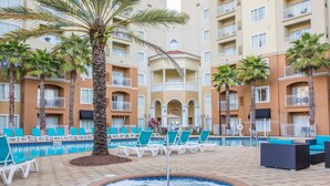 A hotel pool area with lounge chairs, a hot tub, and palm trees.