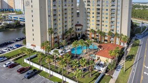 A high-rise hotel with multiple balconies, a swimming pool, and a parking lot.