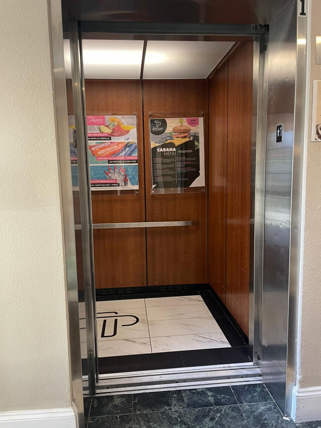 An elevator with wooden doors and a metal handle. There are two posters advertising local businesses.
