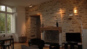 Een woonkamer met een stenen muur, een open haard, een televisie en een eethoek met stoelen en een tafel.