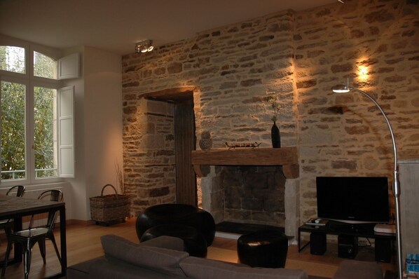 A living room with a stone wall, a fireplace, a television, and a dining area with chairs and a table.