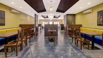 A restaurant with wooden tables and blue cushioned booths, a central serving area, and a stone floor.
