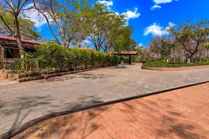 A paved pathway leading to a building with a red roof, surrounded by neatly trimmed hedges and trees. - Club Mahindra Netrang (Netrang)