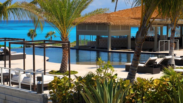 A poolside area with lounge chairs, a thatched-roof structure, and palm trees.