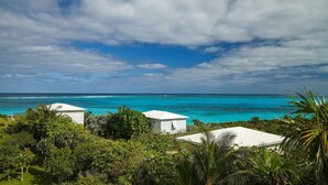 A coastal view with two white buildings surrounded by lush greenery and a turquoise sea under a partly cloudy sky.