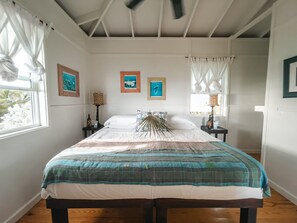 A bedroom with a bed, two nightstands, a ceiling fan, and artwork on the walls. - Cayo Loco 2 1 Bedroom Home (Governor's Harbour)