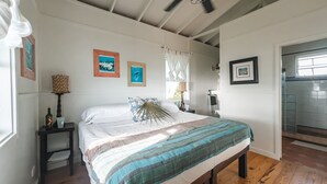 A bedroom with a bed, a ceiling fan, wooden flooring, and framed artwork on the walls.