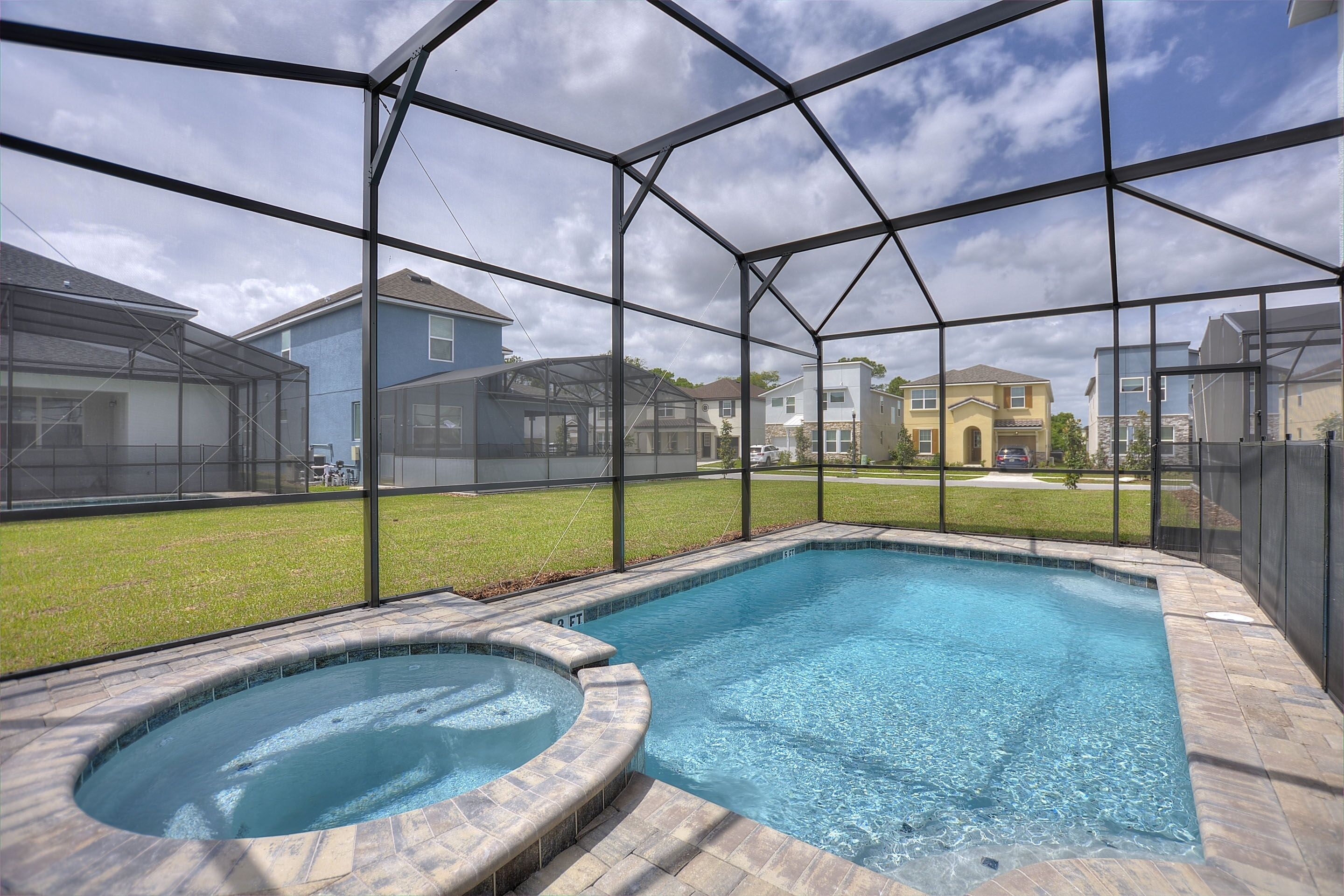 A swimming pool with a hot tub, surrounded by a covered area with a view of neighboring houses.