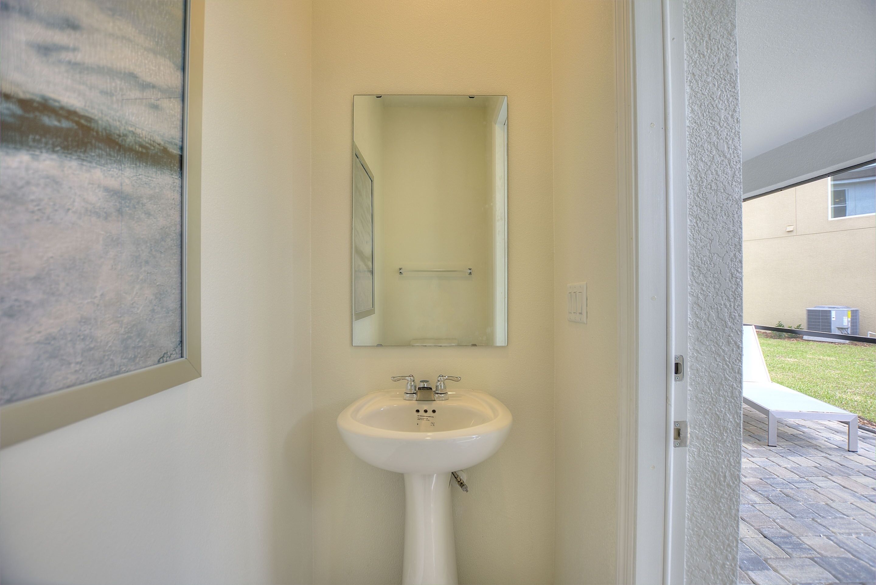 A bathroom with a white sink, a mirror, and a door leading to an outdoor area.