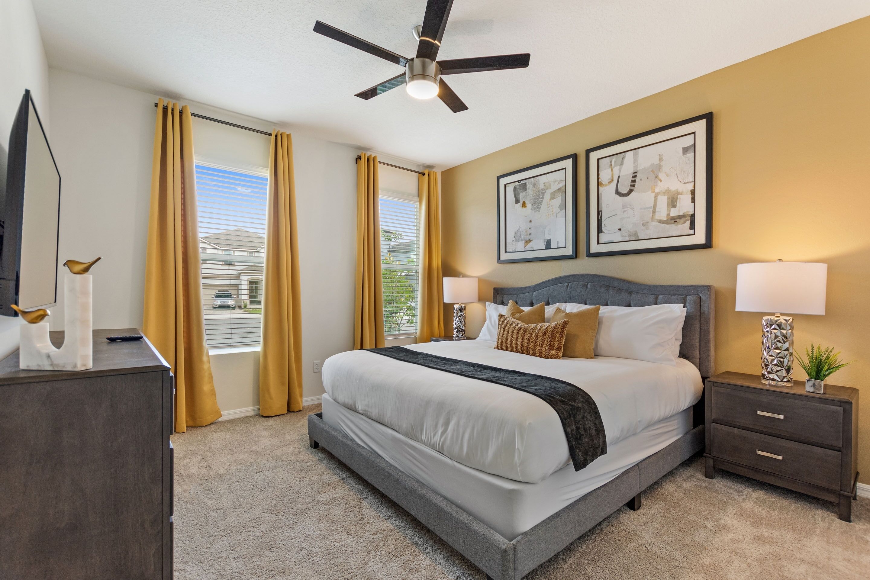 A bedroom with a bed, nightstands, a ceiling fan, and artwork on the wall.