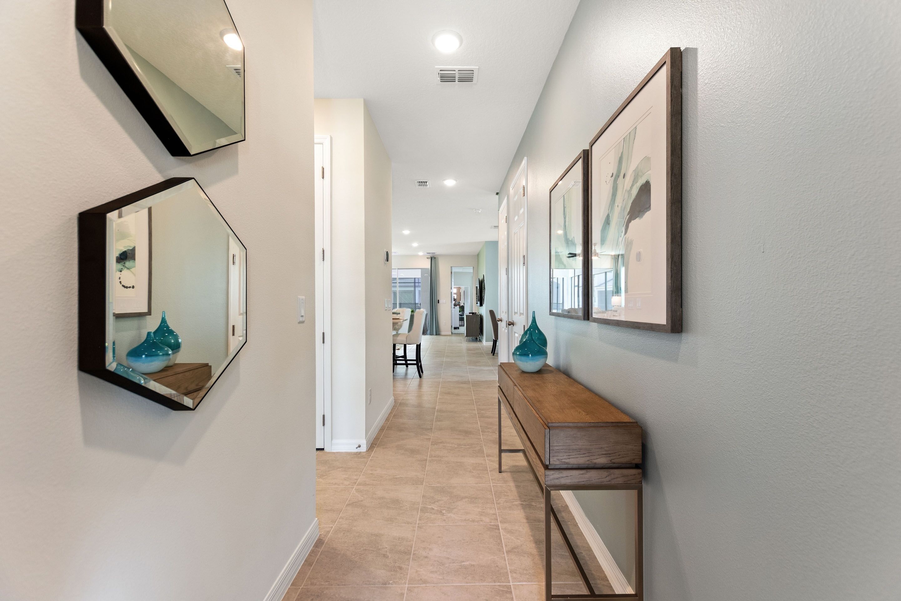 Un couloir avec une console en bois, deux miroirs fixés au mur et un sol carrelé.