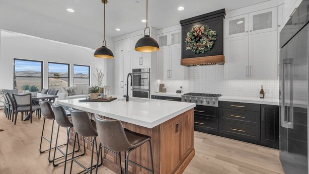 A modern kitchen with a large island, bar stools, and a decorative wreath on the wall.
