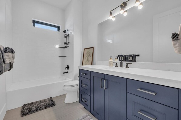 A modern bathroom with a white vanity, dark cabinets, a large mirror, and a shower area.