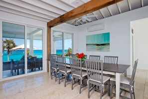 A dining area with a view of the ocean, a ceiling fan, and a painting on the wall. - Sandy Hill Beach House 6 Bedroom Home (Governor's Harbour)