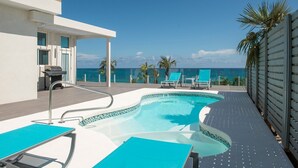 A modern outdoor pool area with a view of the ocean, lounge chairs, and a barbecue grill. - Dream House 3 Bedroom Home (North Palmetto Point)